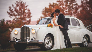 Bride and groom kiss against Bentley
